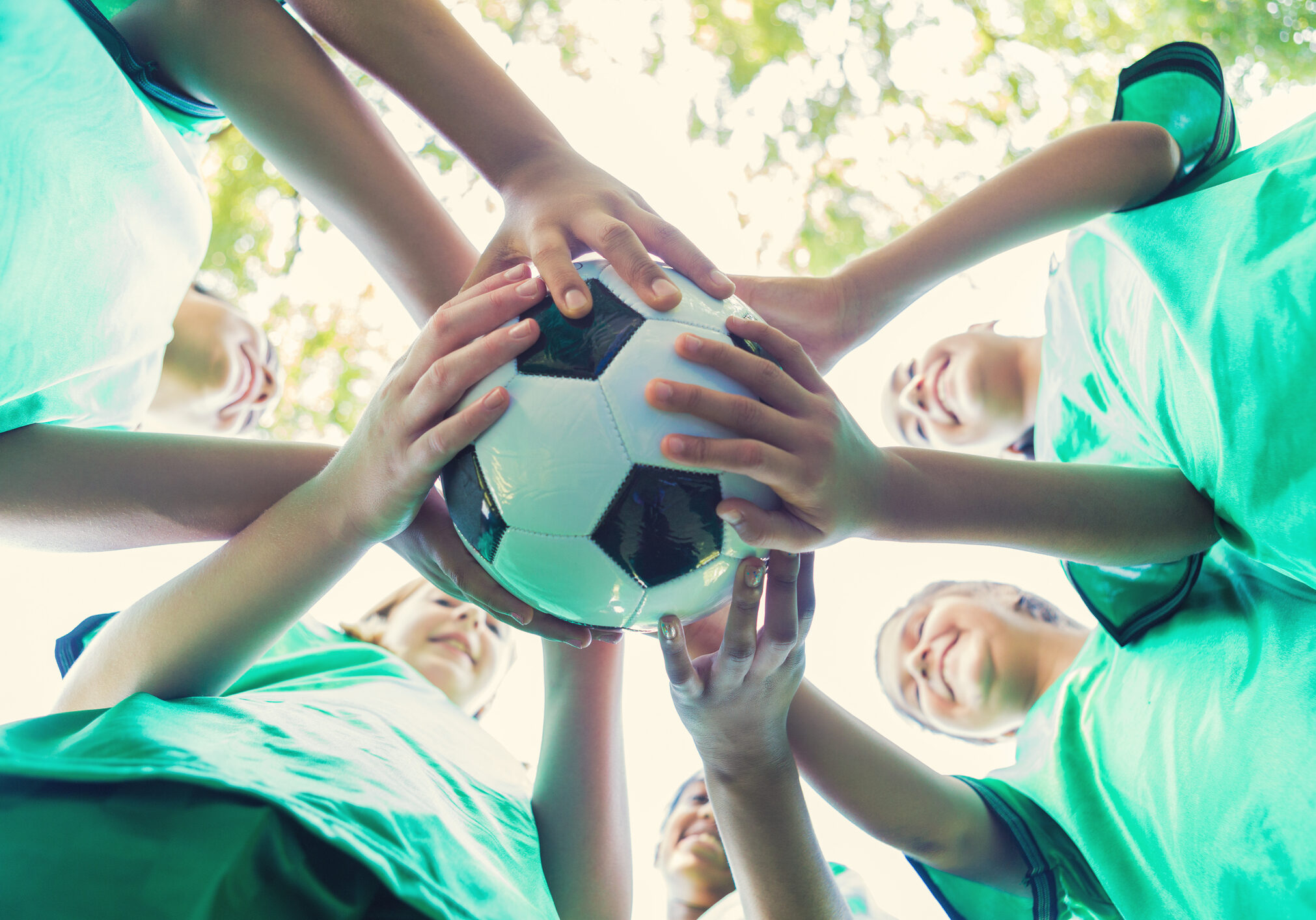 Group of diverse kids huddle together to cheer before their soccer game. Soccer teammates huddle together with their soccer ball to cheer before the game.