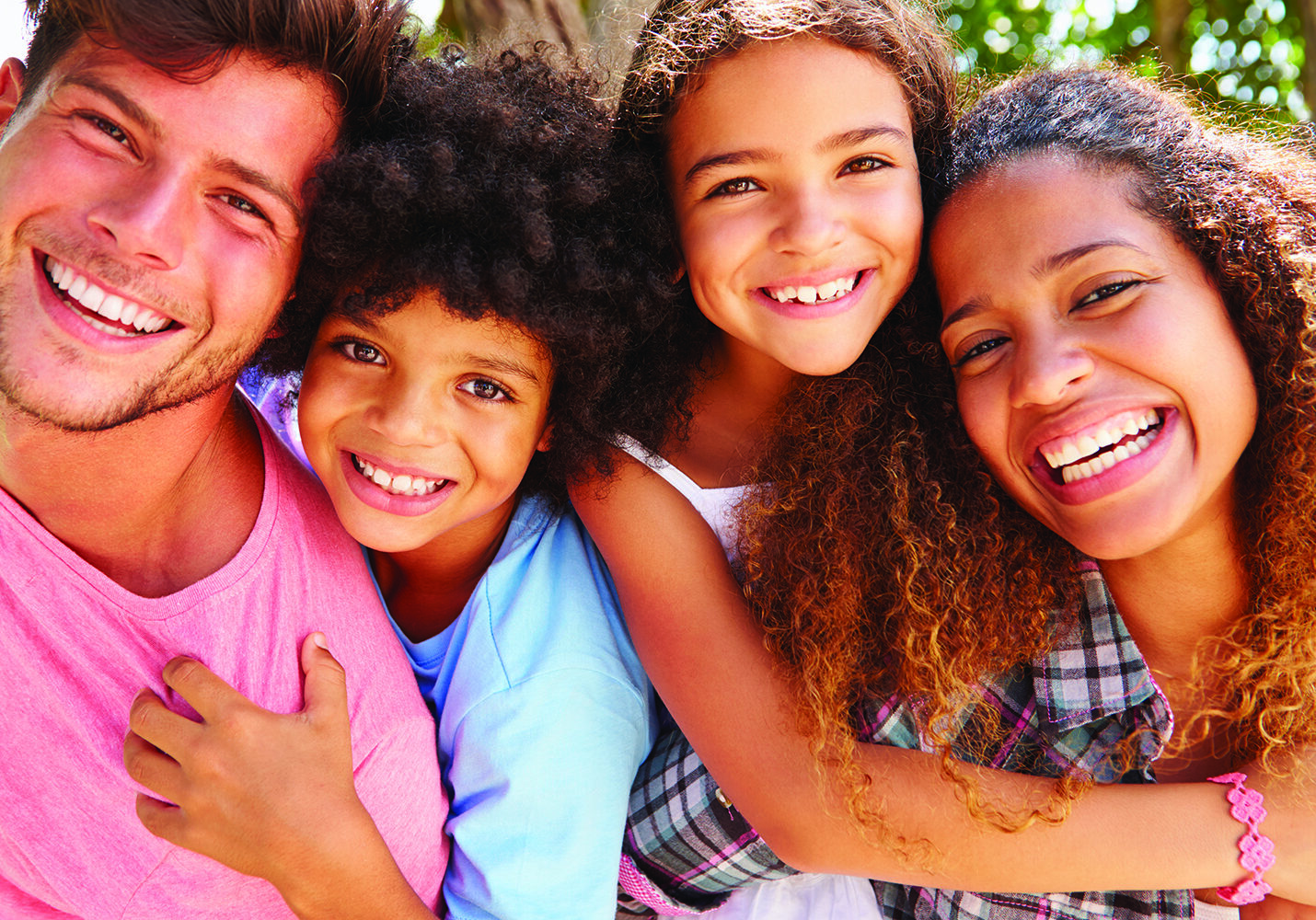 Parents Giving Children Piggyback Ride Outdoors,  Smiling To Camera